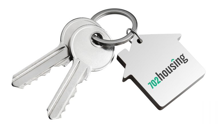Silver house key with a keychain featuring the 702 Housing logo, symbolizing secure and stylish Las Vegas corporate housing.